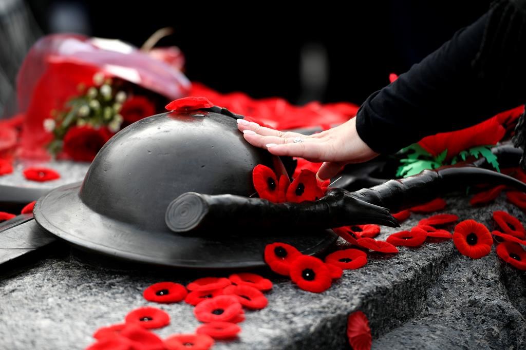 A person touches the helmet on the Tomb of the Unknown Soldier after laying a poppy, at the National War Memorial after the National Remembrance Day Ceremony in Ottawa on Friday, Nov. 11, 2022. THE CANADIAN PRESS/Justin Tang