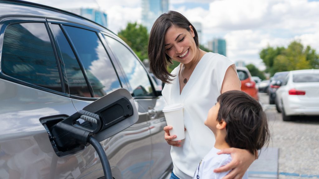 smiling woman and child looking up at her beside silver electric car.