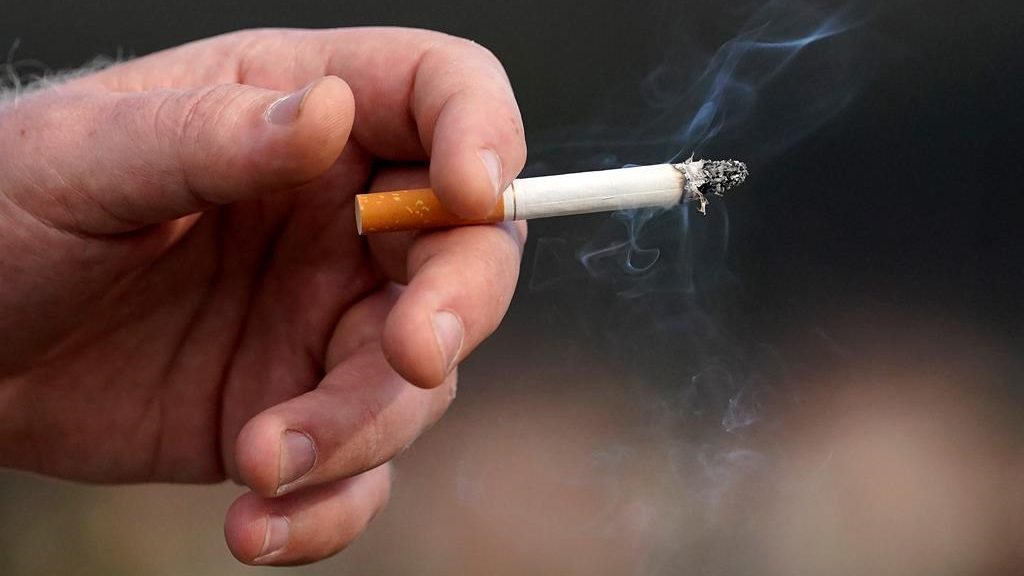 A man holds a lit cigarette while smoking.