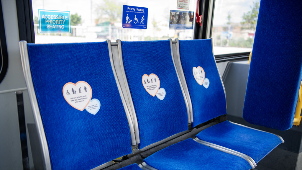 Heart-shaped stickers posted to blue bus seats that say, "This is a priority seat."